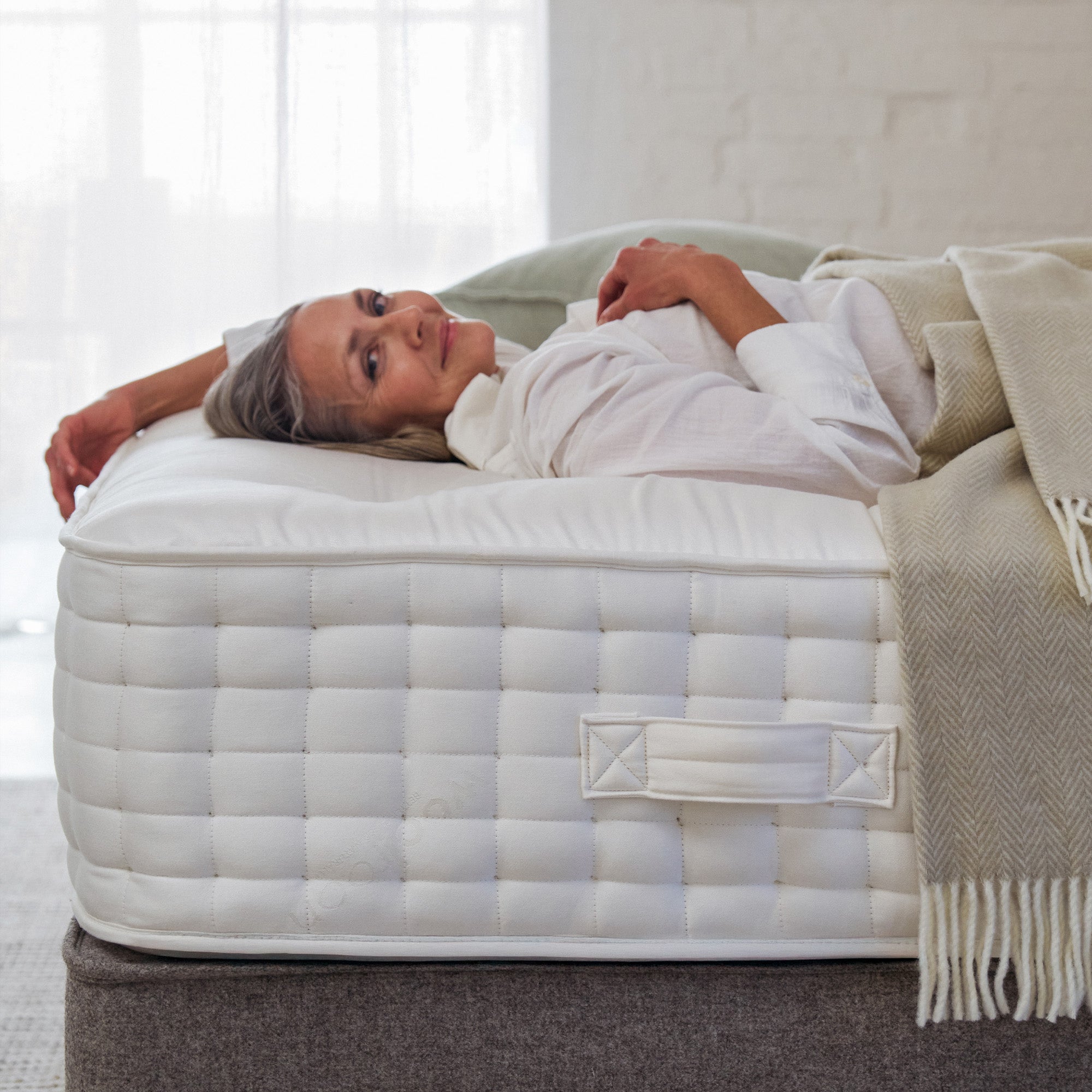 a woman is lying on a Holcombe wool mattress, smiling towards the camera