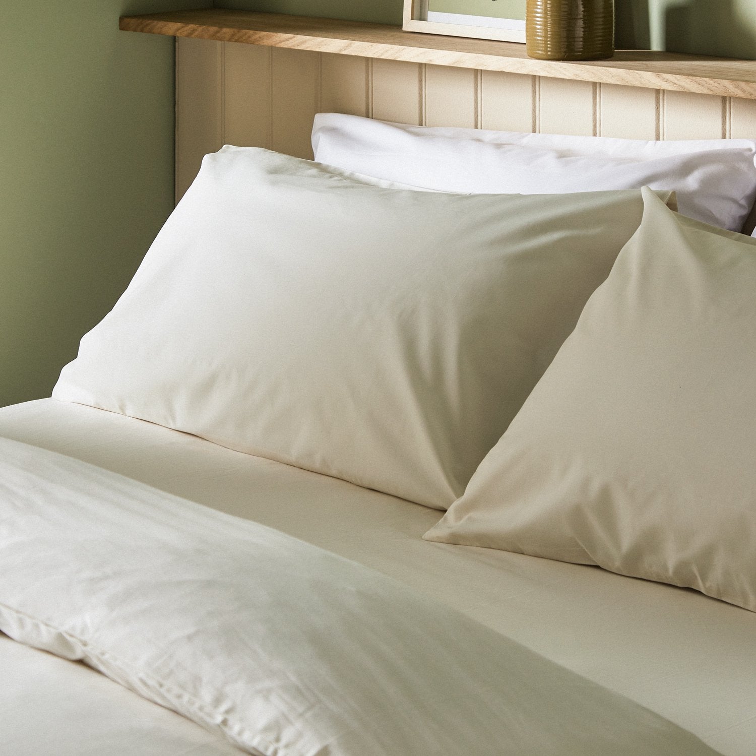 Four pillows on a dressed bed with Arinta Organic Cotton Pillow Cases in Vanilla.
