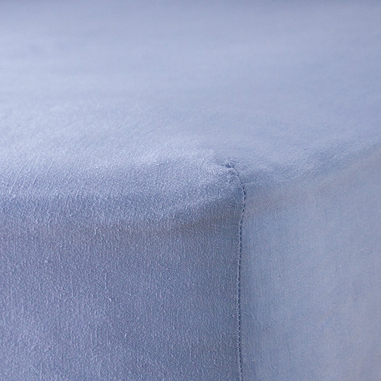 A close up of the corner of a mattress with Woolroom's Mariana Linen Blend Fitted Sheet in Cornflower.