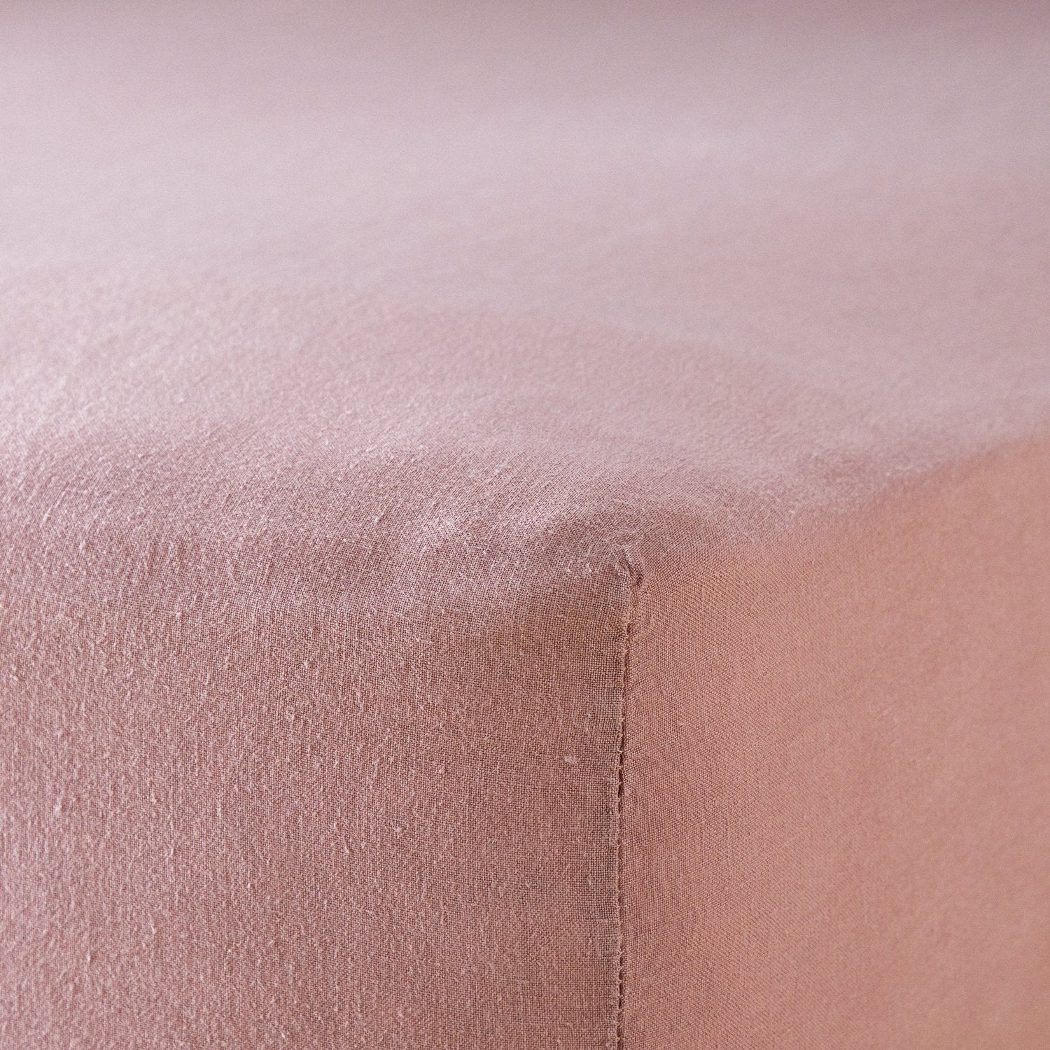 A close up of the corner of a mattress with Woolroom's Mariana Linen Blend Fitted Sheet in Rose.
