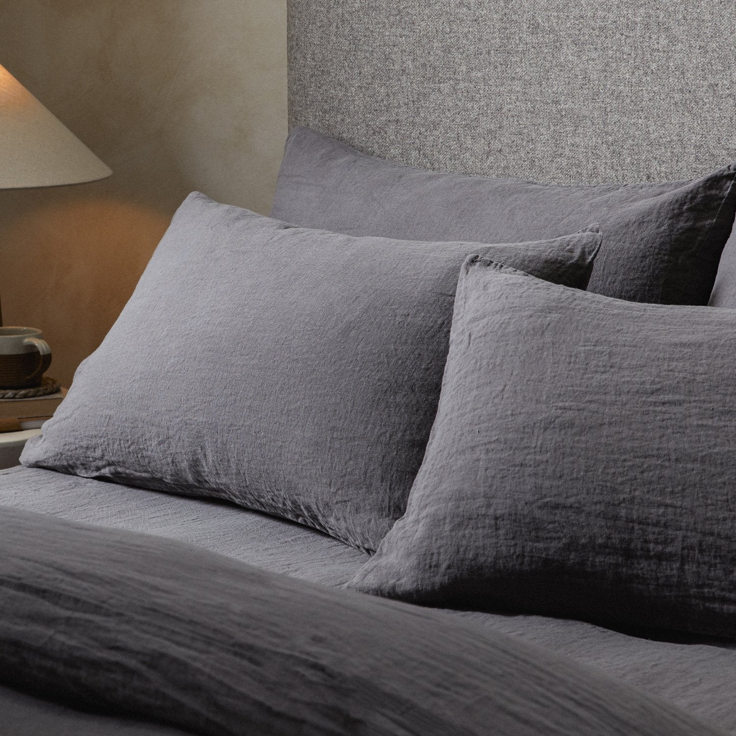 Four pillows on a dressed bed with the Mariana Linen Blend Pillow Cases in Charcoal.
