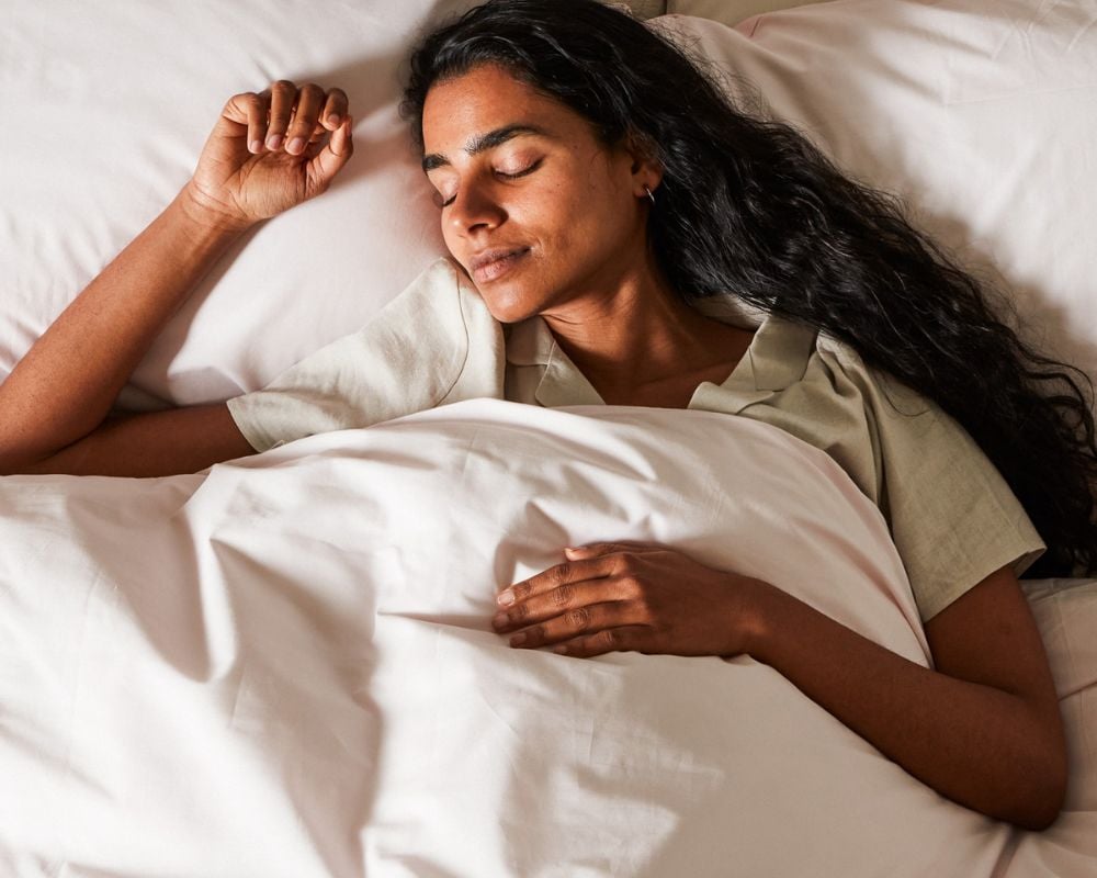 Woman sleeping peacefully under white sheets on a bed.