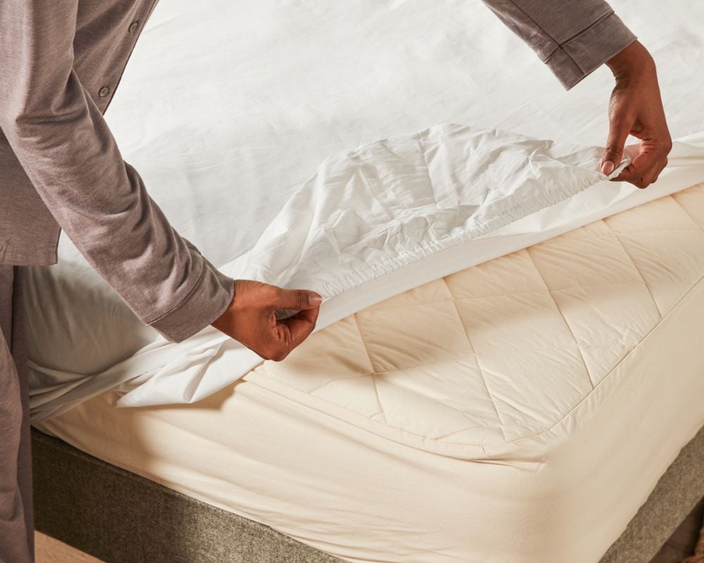 Lady putting on a woolroom sheet on a woolroom bed