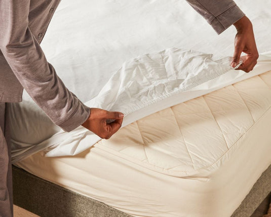 Lady putting on a woolroom sheet on a woolroom bed