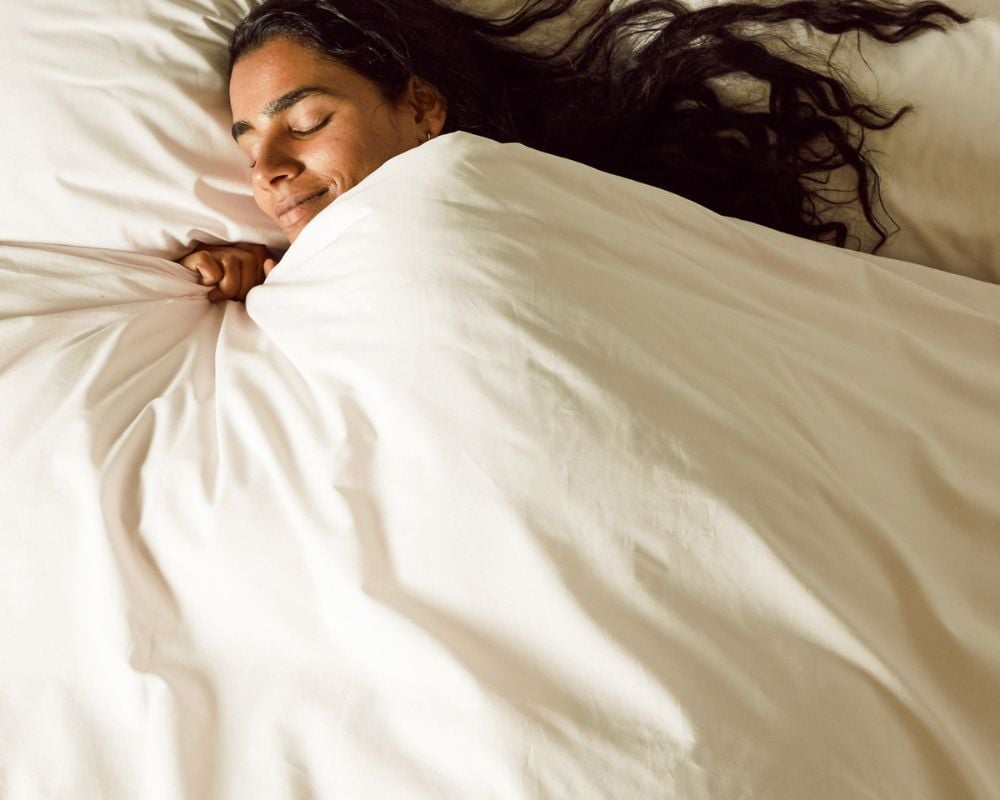 Woman sleeping under white sheets in a bed