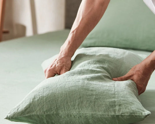 Person adjusting green pillows on a bed