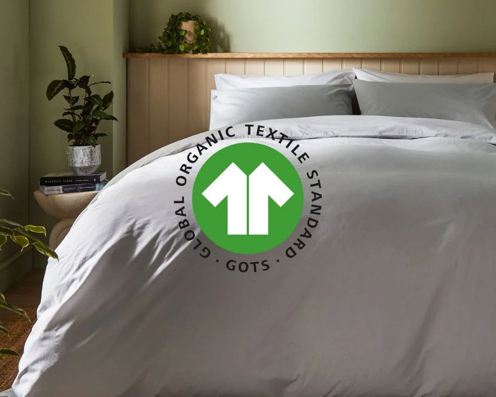 White bedding set with Global Organic Textile Standard logo on a bed in a bedroom setting.