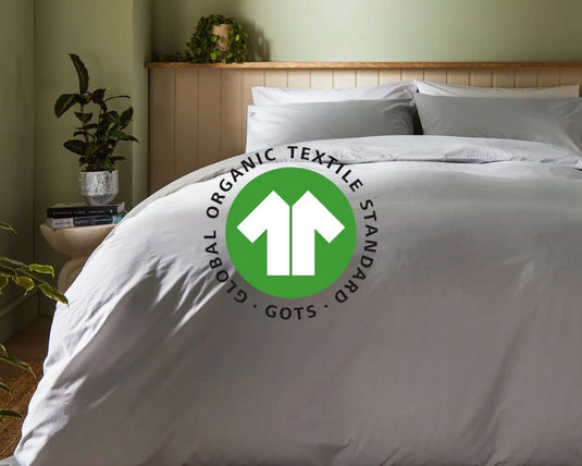 White bedding set with Global Organic Textile Standard logo on a bed in a bedroom setting.