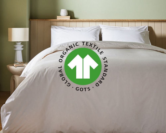 Bed with white bedding featuring the Global Organic Textile Standard logo in a bedroom setting.