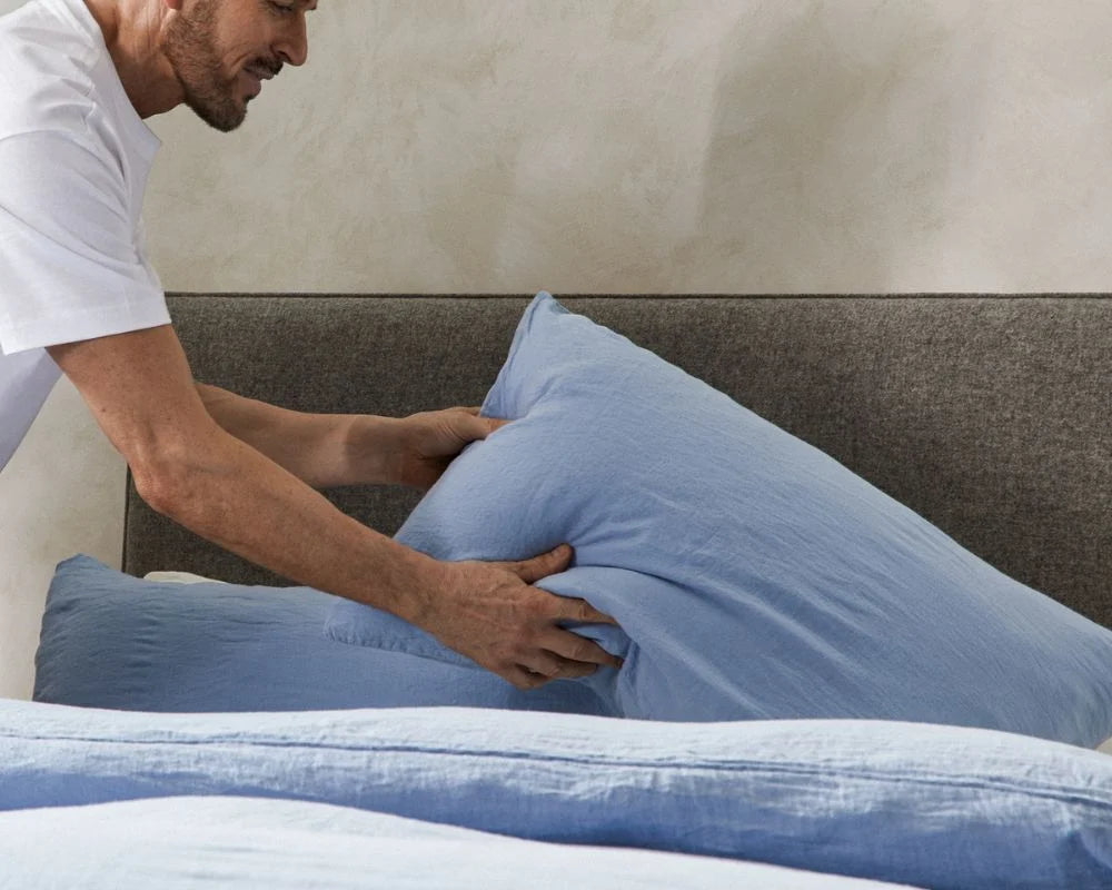 Person adjusting blue pillows on a bed with a neutral wall background