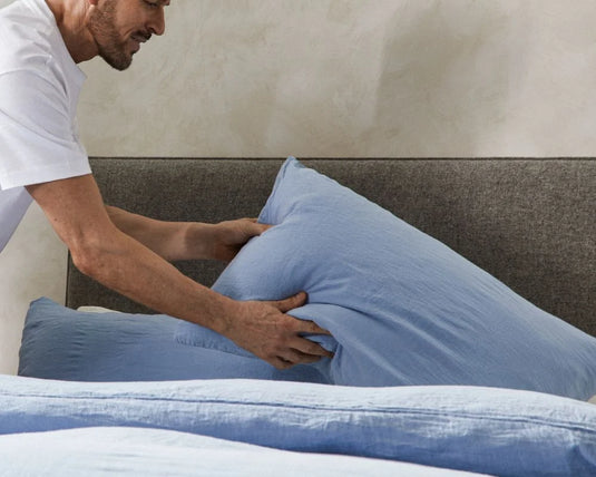 Person adjusting blue pillows on a bed with a neutral wall background