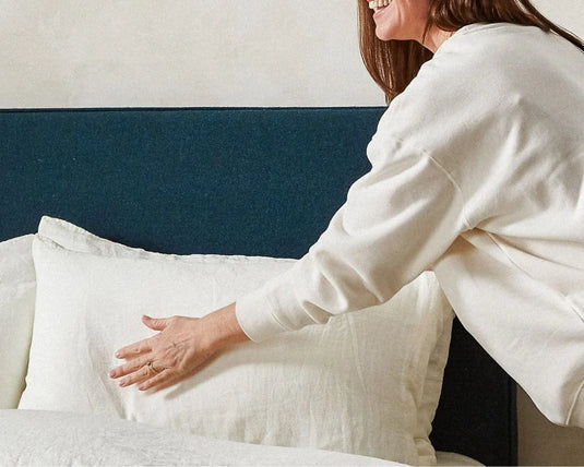 Woman adjusting pillows on a bed with a neutral color scheme