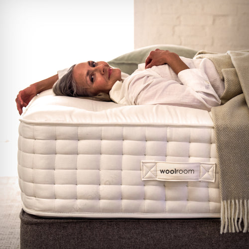 A man hand teasing wool on top of a mattress, in Woolroom's factory
