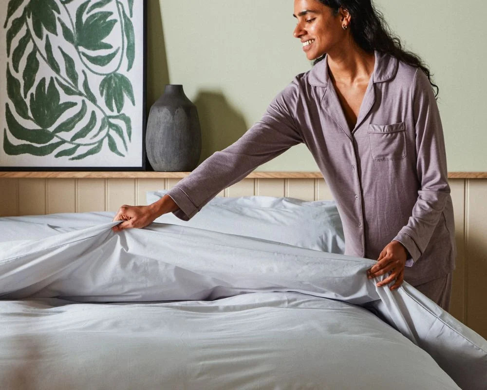 Woman in a bedroom setting, adjusting white bedding.