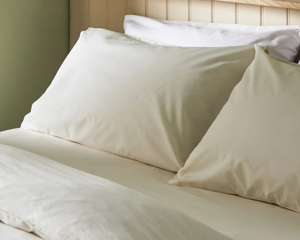 Beige bed sheets and pillows on a bed with a wooden headboard.
