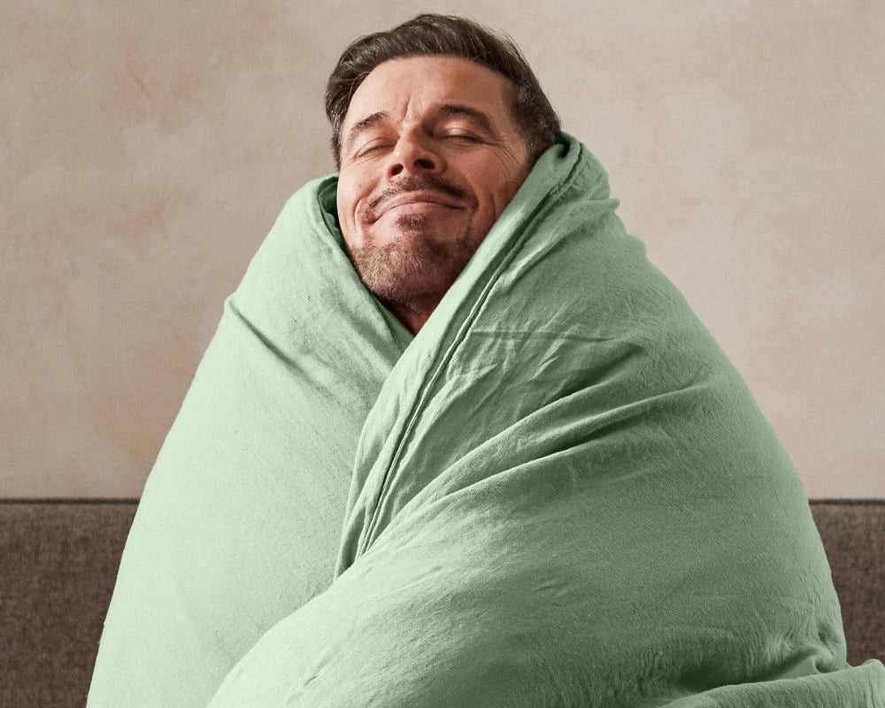 Man wrapped in a green blanket against a beige wall
