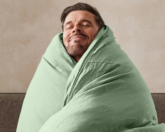 Man wrapped in a green blanket against a beige wall