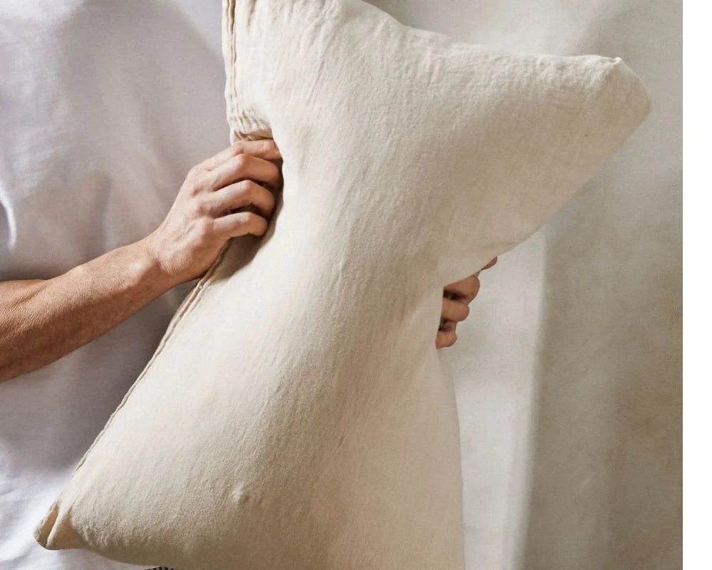 Person holding a large white pillow against a neutral background