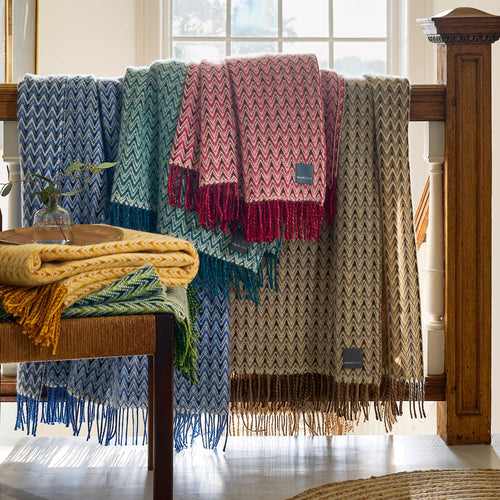 A collection of blue, green, red, beige and yellow wool throws draped over a wooden banister in a home.